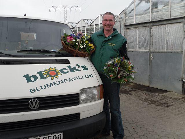 Jens-Olaf Block steht am Firmenfahrzeug mit Blumensträußen in der Hand